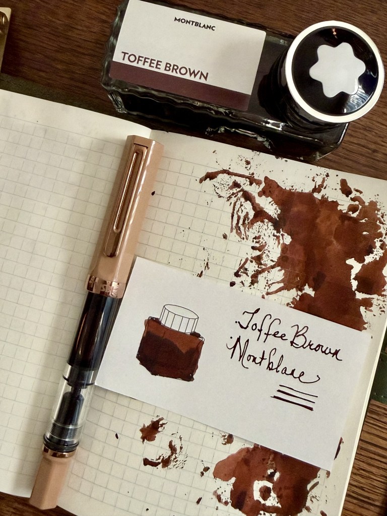 A flat lay of a Montblanc ink bottle labeled 'Toffee Brown,' a fountain pen, and a sketch on grid paper featuring a drawing of the ink bottle with brown ink splatters around.